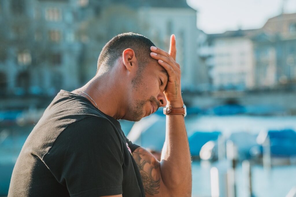 A man with his hand on his head and his eyes closed with a blurred background.